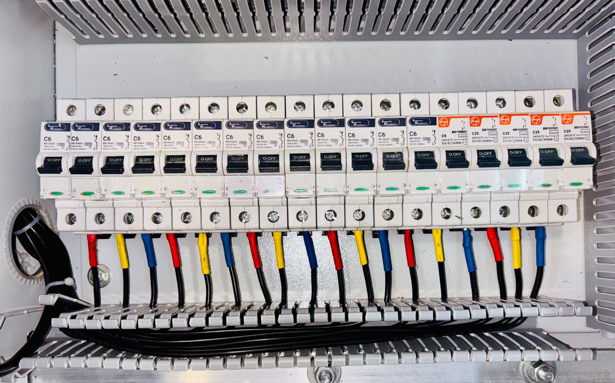 Quadro de distribuição trifásico com disjuntores alinhados em trilho e cabos identificados por cor de fase