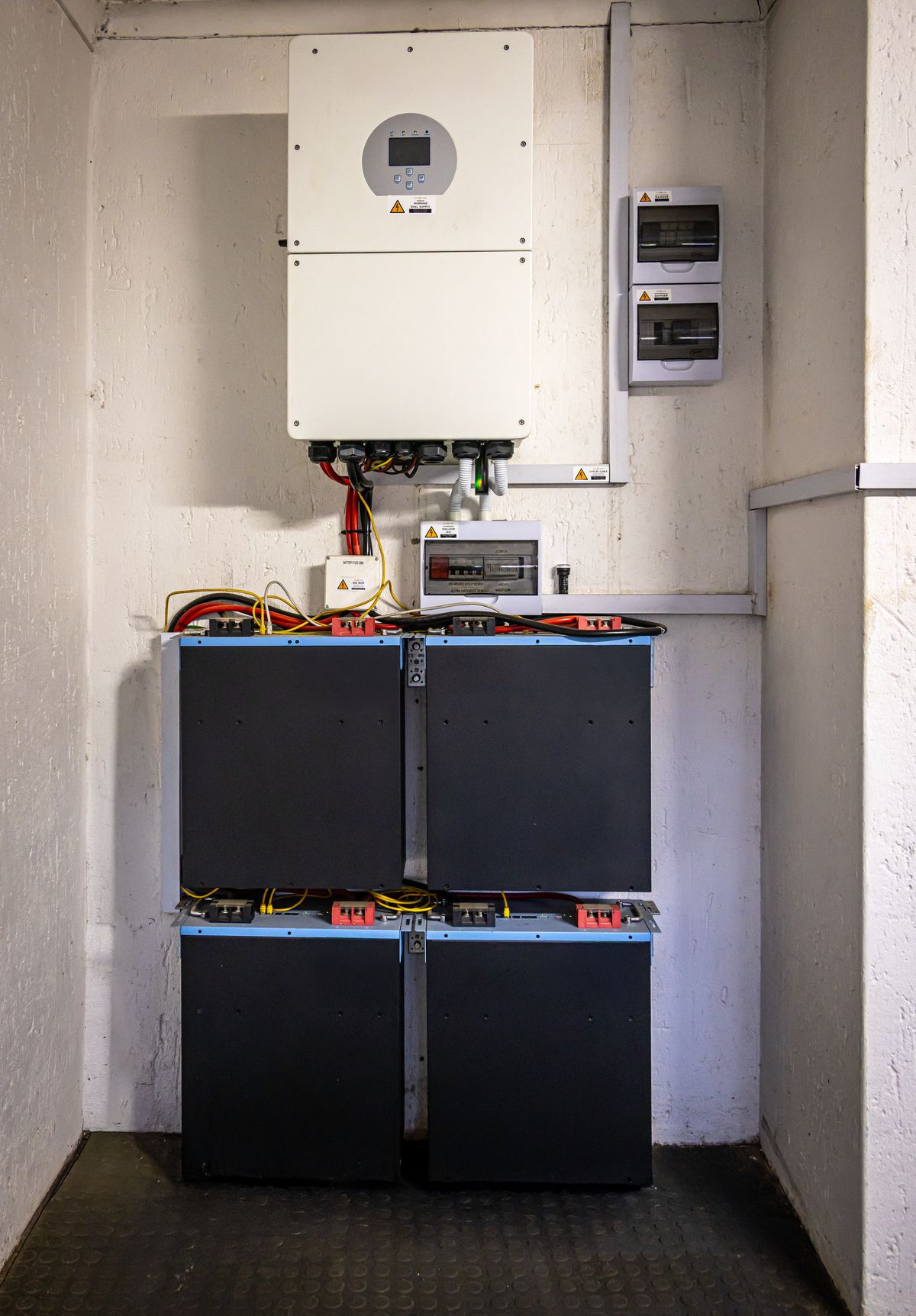 Instalação fotovoltaica com inversor, banco de baterias e quadros de proteção CC e CA na parede