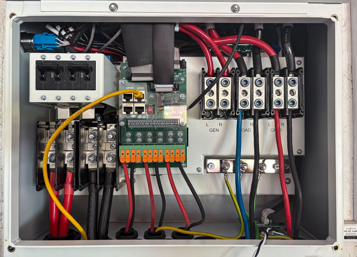 Interior de quadro de transferência com barramentos e bornes identificados para rede, gerador e carga