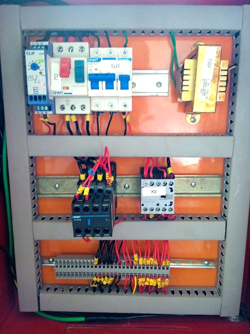 Interior do painel de comando com placa de montagem laranja, relé temporizador, disjuntor-motor, disjuntores em trilho DIN, transformador de comando, contatores e régua de bornes com fios ferrulados