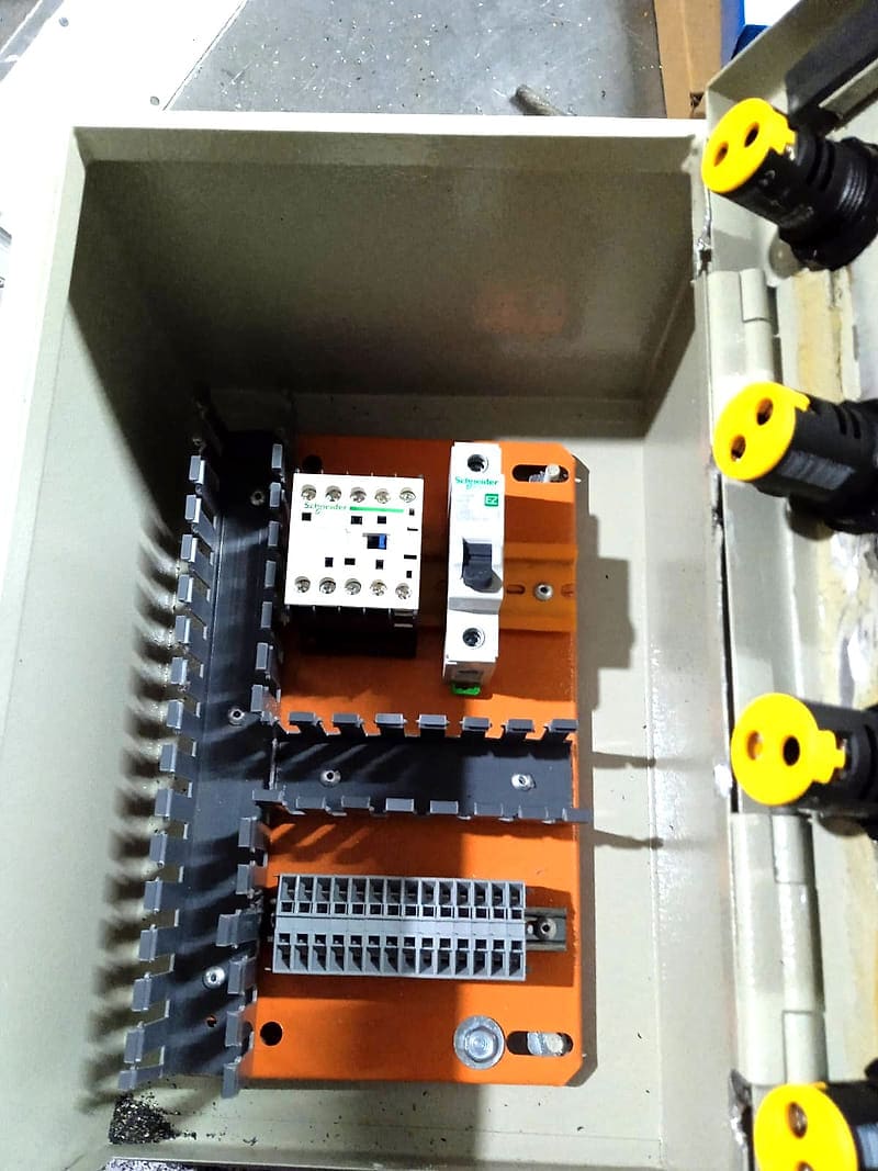 Caixa metálica aberta com placa de montagem laranja, canaletas de fiação, contator e disjuntor em trilho DIN e régua de bornes